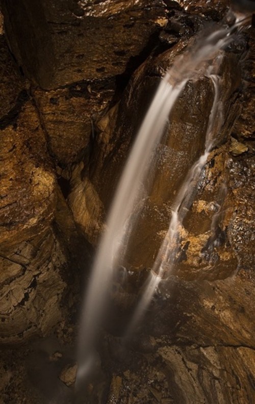 A cascading waterfall flows down rocky cliffs into a dark, secluded pool below.