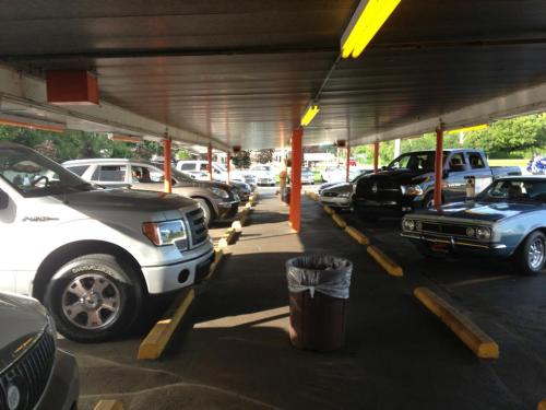 A parking lot with various cars under a covered area, featuring a trash can in the center.
