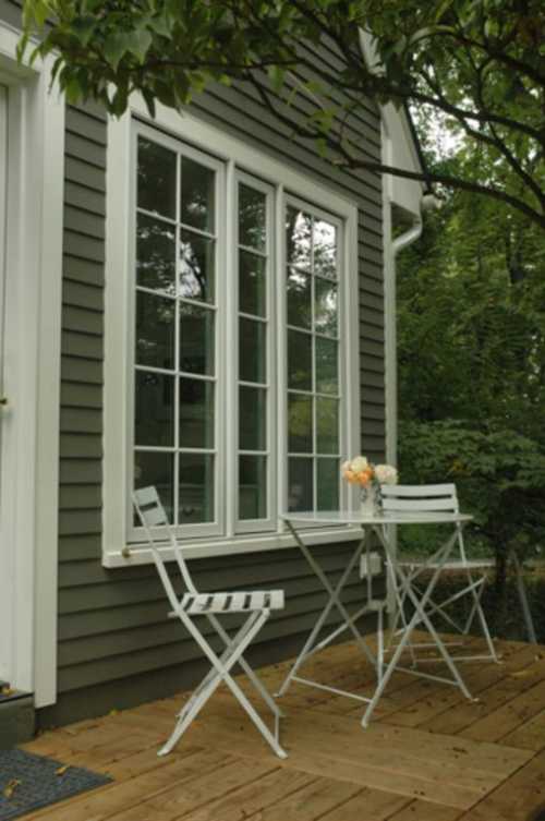 A cozy outdoor seating area with two white chairs and a small table, surrounded by greenery.