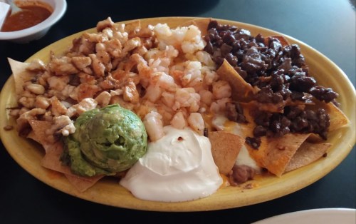 A colorful plate of nachos topped with grilled chicken, shrimp, black beans, guacamole, and sour cream.