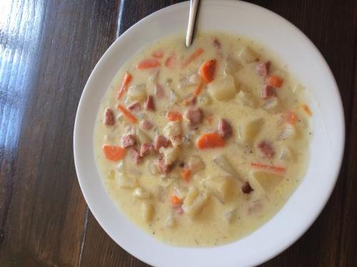 A bowl of creamy soup with diced potatoes, carrots, and chunks of meat, served on a wooden table.