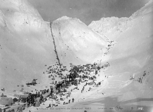 Historic black-and-white photo of Chilkoot Pass, featuring a large group of people and tents in a snowy landscape.