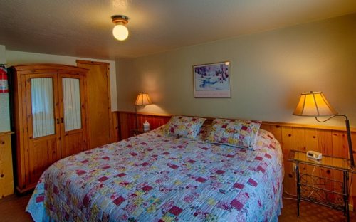 Cozy bedroom with a quilted bedspread, wooden furniture, and warm lighting from bedside lamps.