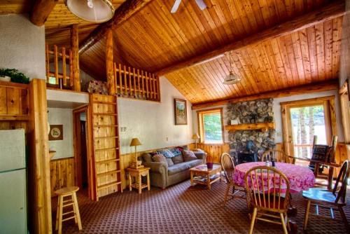 Cozy cabin interior with wooden beams, a living area, dining table, and a staircase leading to a loft.