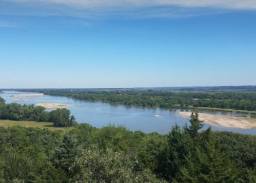 A scenic view of a river winding through lush greenery under a clear blue sky.