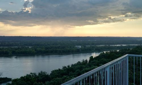 A scenic view of a river surrounded by lush greenery under a cloudy sky at sunset.