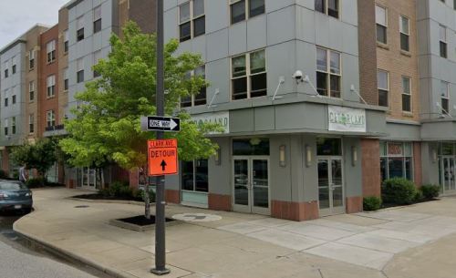 A street corner featuring a modern building, a traffic sign, and a tree in a city setting.
