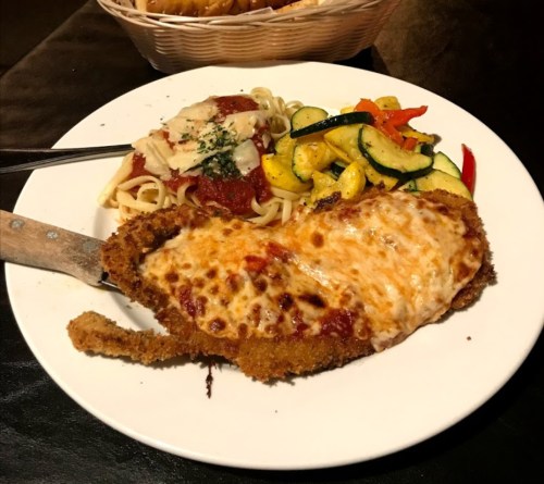 A plate with breaded chicken topped with melted cheese, spaghetti in marinara sauce, and sautéed vegetables.