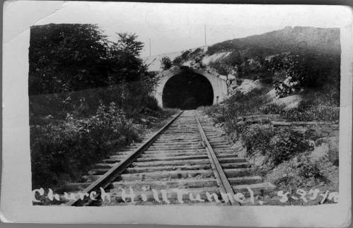 Black and white photo of Church Hill Tunnel entrance with railway tracks leading into the tunnel, surrounded by greenery.
