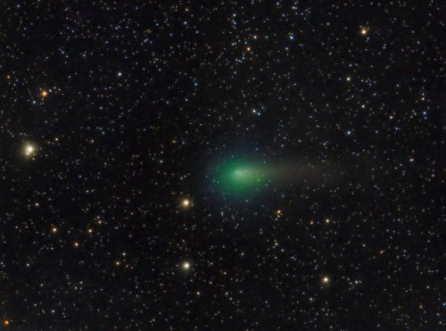 A bright green comet with a long tail, surrounded by a field of stars in a dark night sky.