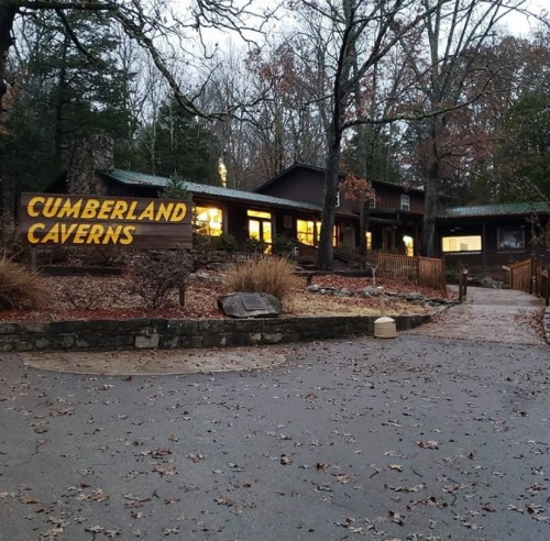 Cumberland Caverns entrance with a wooden sign, surrounded by trees and a pathway leading to the building.