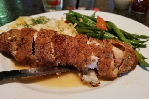 A plate of crispy chicken, pasta, and sautéed green beans with carrots, garnished with herbs.