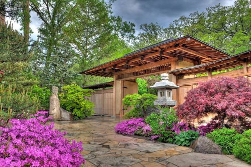 A serene garden with vibrant flowers, a stone lantern, and a wooden gate surrounded by lush greenery.