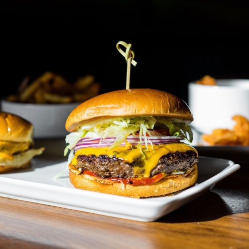 A juicy cheeseburger with lettuce, tomato, onions, and cheese on a toasted bun, served with sides in the background.