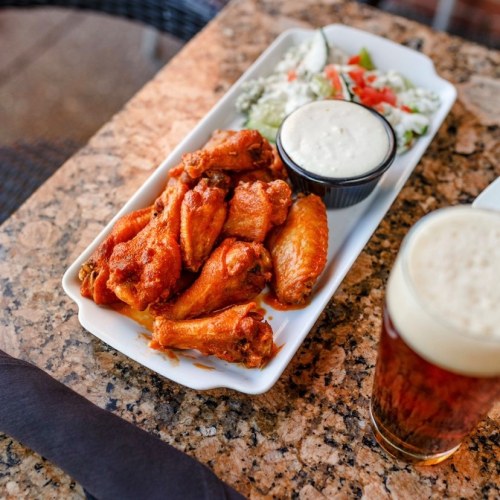 A platter of spicy chicken wings with dipping sauce, accompanied by a side salad and a glass of beer on a table.