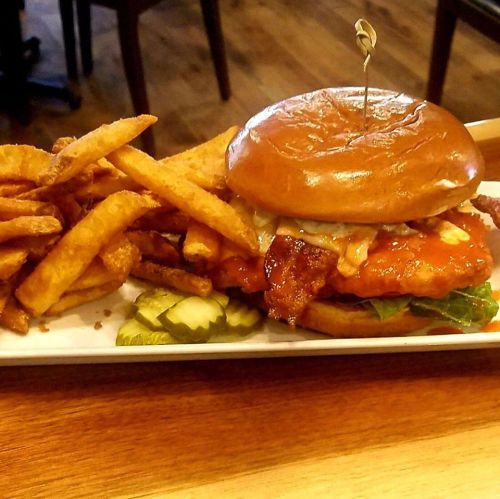A crispy chicken sandwich topped with bacon and lettuce, served with a side of golden fries and pickles.