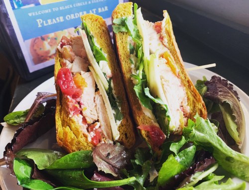 A close-up of a sandwich with turkey, lettuce, and tomato, served with a side of mixed greens on a plate.