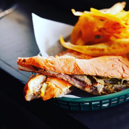 A close-up of a sandwich with layers of meat and mustard, served with crispy potato chips on the side.
