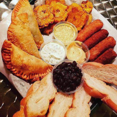 A platter featuring empanadas, tostones, dipping sauces, black beans, and slices of bread.