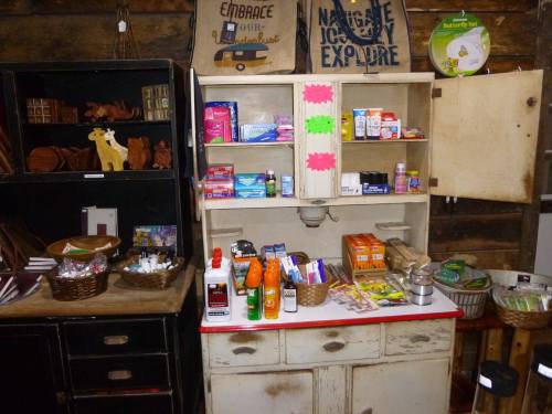 A vintage wooden cabinet filled with various household items, toiletries, and snacks, set in a rustic environment.