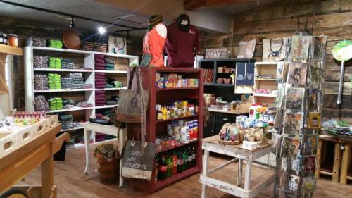 A cozy store interior featuring shelves of clothing, snacks, and various merchandise in a rustic setting.