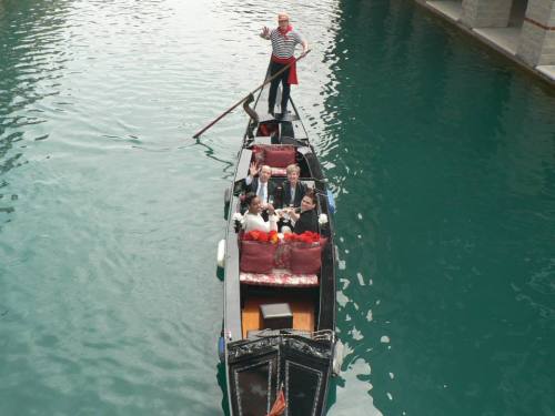 A gondola with passengers smiles as the gondolier waves, gliding through calm turquoise water.