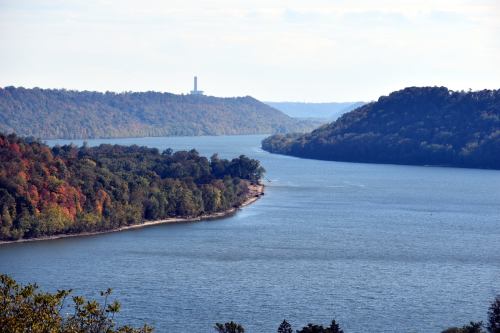 A scenic view of a winding river surrounded by lush green and autumn-colored hills under a clear sky.