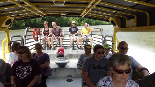 A group of people sitting on a boat, enjoying a scenic ride on a river surrounded by greenery.
