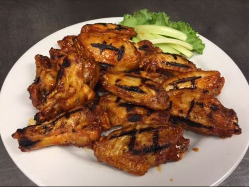 A plate of grilled chicken wings with a glossy glaze, served with lettuce and cucumber slices on the side.