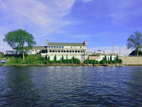 A waterfront view of a building with a sign reading "Sportsman Inn," surrounded by greenery and a clear blue sky.