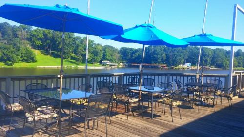Outdoor dining area with blue umbrellas overlooking a calm lake and green trees in the background.