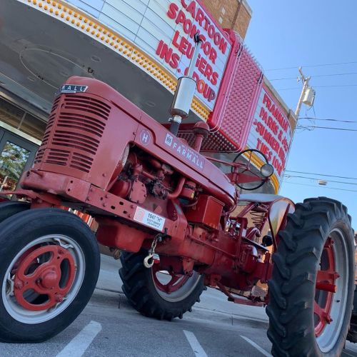 A vintage red Farmall tractor parked in front of a retro theater marquee.