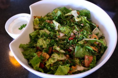A fresh salad with mixed greens, tomatoes, and herbs, served with a side of dressing in a small bowl.