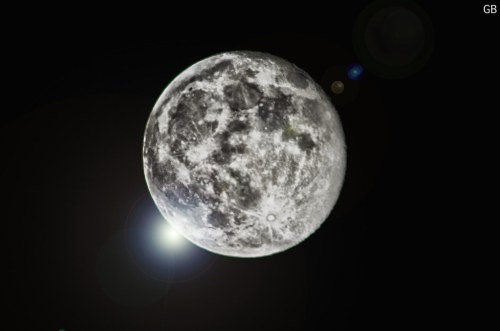 A bright, detailed full moon against a dark sky, with lens flare effects adding a touch of light.
