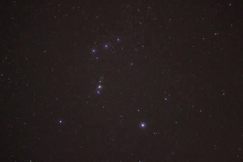 A night sky filled with stars, prominently featuring the Orion constellation.