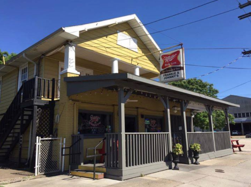 A yellow two-story building with a porch, featuring a sign for "Frankie & Johnny's" and outdoor seating.
