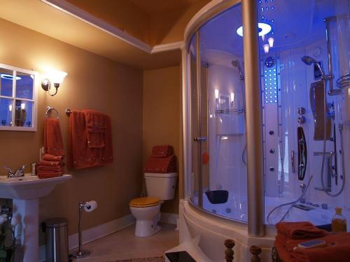 A modern bathroom featuring a glass shower, toilet, sink, and orange towels, illuminated with soft blue lighting.