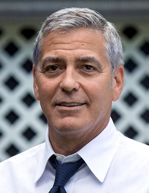 A man with gray hair and a white shirt smiles, standing in front of a lattice background.