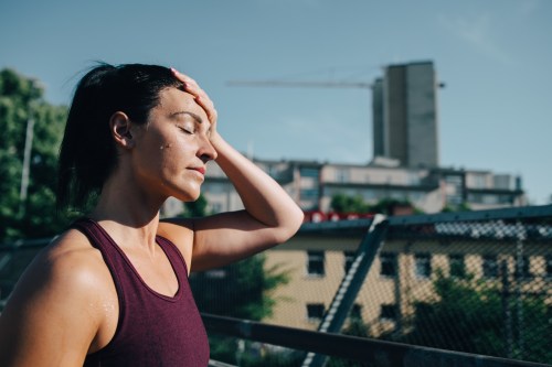A woman wipes sweat from her forehead while exercising outdoors, with a cityscape and construction in the background.