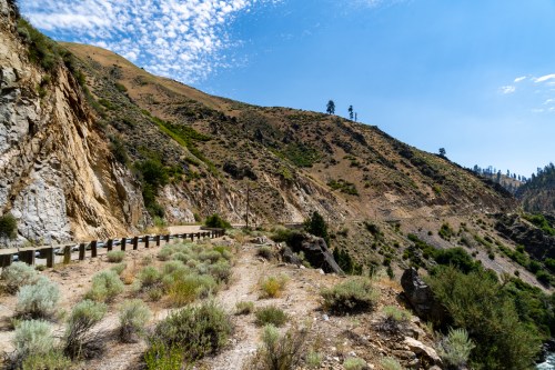 A winding road along a rocky hillside, surrounded by sparse vegetation and under a clear blue sky.