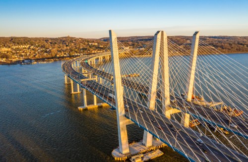 Aerial view of a modern cable-stayed bridge spanning a river, with sunlight illuminating its structure and surrounding landscape.