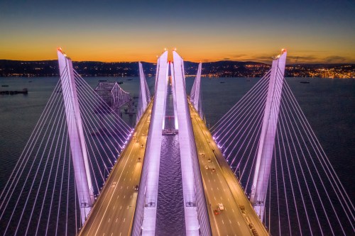 Aerial view of a illuminated cable-stayed bridge at sunset, with traffic and water below.