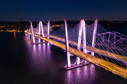 Aerial view of a brightly lit suspension bridge at night, reflecting in the water below.