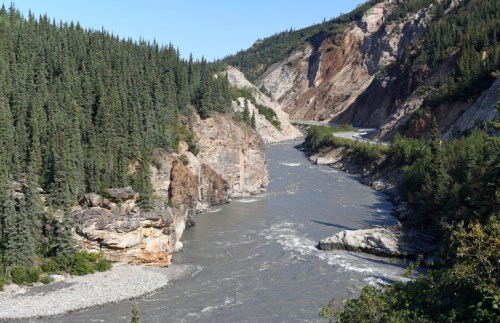 A winding river flows through a rocky canyon surrounded by dense green forests under a clear blue sky.