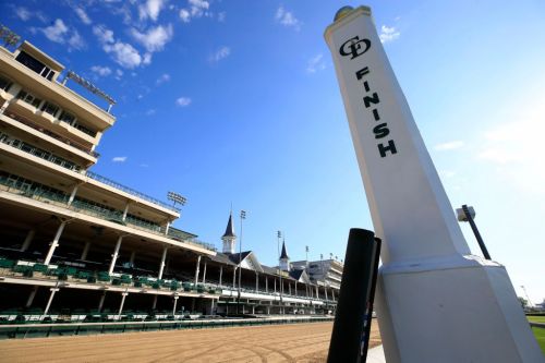 A finish line marker at a racetrack, with grandstands and spires in the background under a clear blue sky.