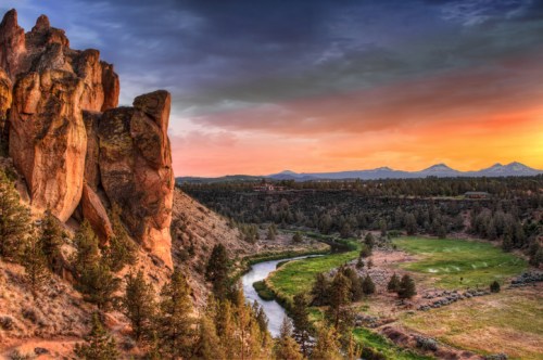 A scenic view of a river winding through a valley, framed by rocky cliffs and a colorful sunset sky.