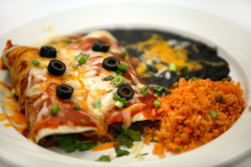 A plate of enchiladas topped with olives, served with rice and black beans, garnished with green onions and cilantro.