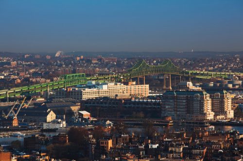 Aerial view of a green bridge spanning over a cityscape with buildings and a harbor in the foreground.