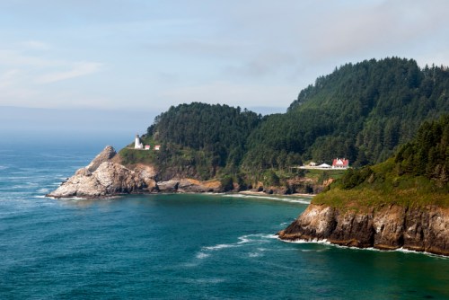 A scenic coastal view featuring a lighthouse on a rocky cliff, surrounded by lush greenery and calm blue waters.