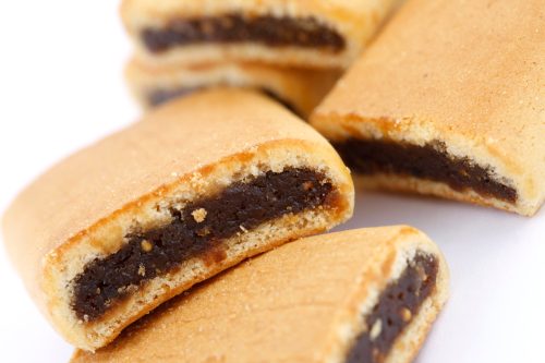 Close-up of rectangular cookies with a dark filling, stacked on a white background.